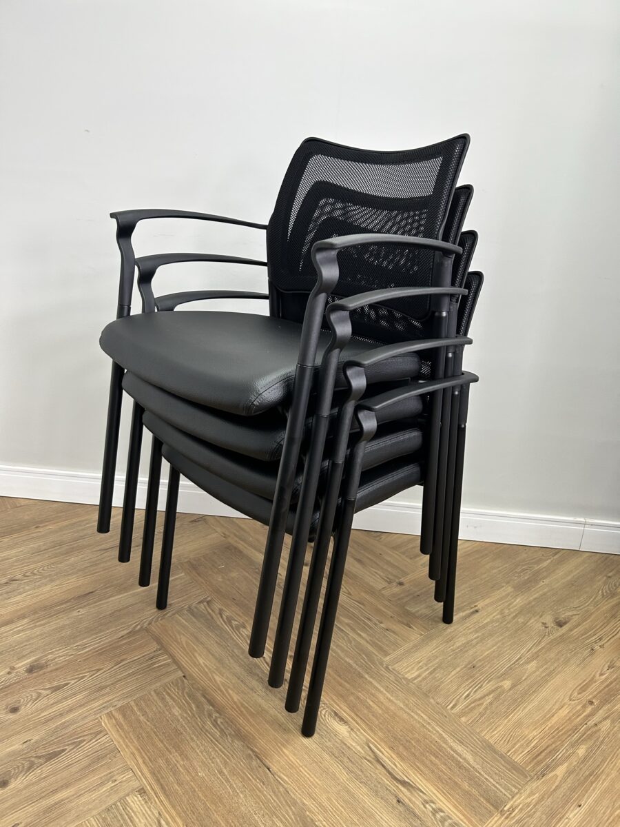 Demonstração da praticidade da Cadeira Empilhável com Tela para Sala de Treinamento: quatro unidades do modelo Force (Duratta) empilhadas, mostrando a otimização de espaço. Cadeiras pretas com assento em couro sintético e encosto mesh, perfeitas para auditórios e áreas multifuncionais.