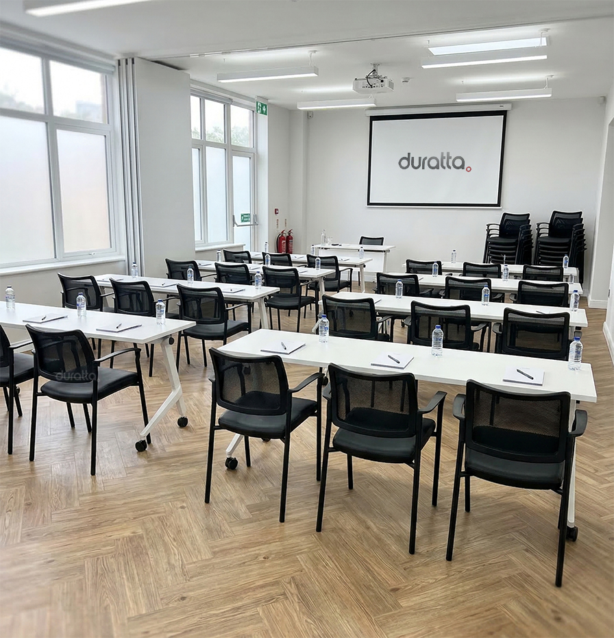 Sala de treinamento corporativa moderna equipada com cadeiras Force da Duratta com encosto em tela. Ambiente moderno e funcional em São Paulo, mostrando a aplicação prática do design empilhável e o conforto da tela mesh com o logo Duratta na tela do projetor.